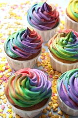 Delicious cupcakes with colorful cream and confetti on light table, closeup