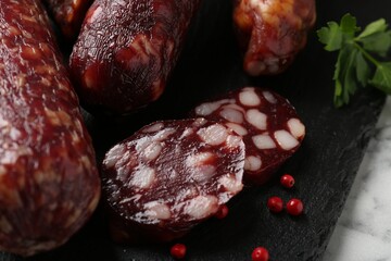Different smoked sausages and peppercorns on light table, closeup