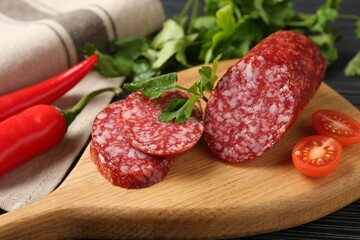 Cut smoked sausage, parsley and tomatoes on black wooden table, closeup