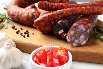 Different smoked sausages, chili pepper and garlic on white table, closeup