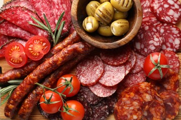 Different smoked sausages slices, olives, tomatoes and rosemary on table, closeup