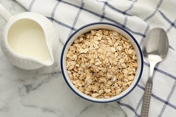 Tasty oatmeal in bowl and milk served on white marble table, flat lay
