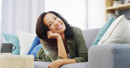 Happy woman, portrait and relax with coffee on sofa for holiday, weekend or comfort at home. Face, female person and lying with smile in joy for break, rest or morning on living room couch at house