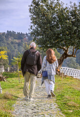 Fototapeta premium A man and a woman walk along a stone path to a tree and a white wooden bridge. Rear view