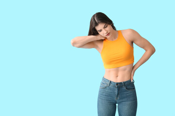 Beautiful young woman suffering from back pain on blue background