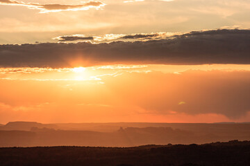 The sun is setting over a mountain range, casting a warm glow over the landscape
