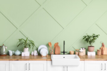 Blurred view of modern kitchen with counters, sink and utensils near green wall