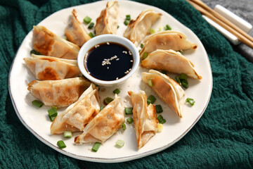Plate with fried Japanese gyoza and bowl of soy sauce on black background, closeup