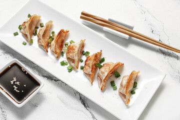 Plate with fried Japanese gyoza and bowl of soy sauce on white background