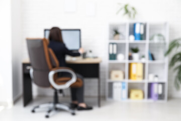 Female office worker sitting on armchair at workplace in light office, blurred view