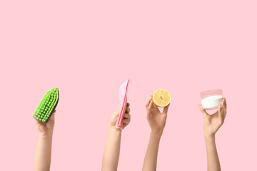 Female hands holding cleaning brush, rag, lemon and jar with cleaning agent on pink background