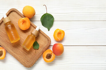 Bottles of cosmetic oil with fresh apricots on white wooden background