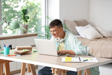 Teenage boy studying with laptop at table in bedroom
