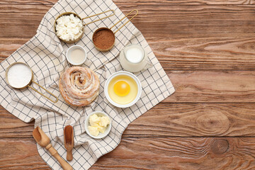 Sweet cinnamon roll and different ingredients on wooden background