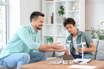 Teenage boy with light bulb and his father talking about wind turbine model at home