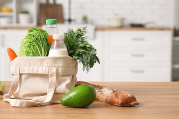 Shopping bag with different fresh products on wooden table in kitchen
