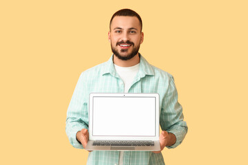 Young man with blank laptop on orange background