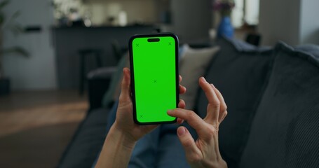A woman uses a mobile phone with green screen lying on the couch at home, close-up of her hands, an unrecognizable person