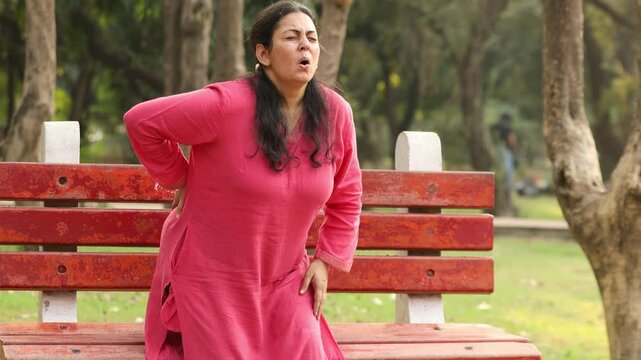Indian woman suffering from back pain outdoor at park. Mature lady having pain in her spine, Aging process.