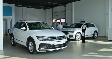 Naklejka premium The car dealership manager talks to the customer standing near the car in the showroom