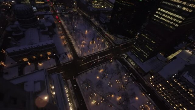 FPV drone pushes forward from rooftop of Sun Life building, descending smoothly to snowy streets of Square Dorchester, Montreal Downtown with stunning night views.