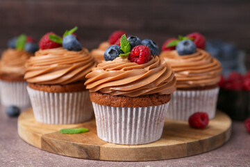 Tasty cupcakes with chocolate cream and berries on brown table, closeup
