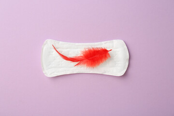 Menstrual pad with red feather on lilac background, top view