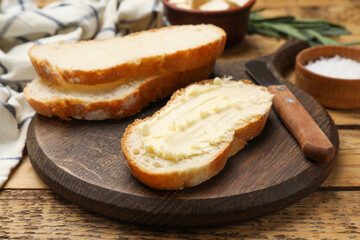 Fresh bread with butter and knife on wooden table, closeup
