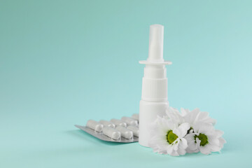 Allergy treatment. Nasal spray, pills and flowers on light blue background. Space for text