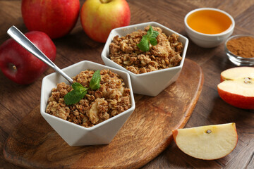 Tasty apple crisp in bowls, ingredients and spoon on wooden table, closeup