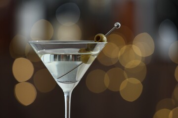 Martini cocktail with olive in glass on blurred background, closeup. Bokeh effect