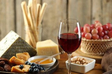 Red wine and different snacks served on wooden table, closeup