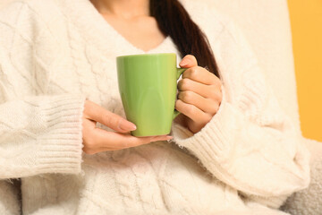 Young Asian woman with cup of hot tea on yellow background, closeup