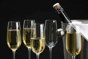 Bottle of sparkling wine in cooler bucket and glasses against black background, closeup