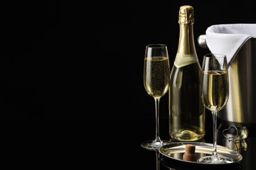 Bottle of sparkling wine, glasses and cooler bucket on black mirror surface. Space for text