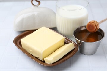 Fresh milk in glass, honey and butter on white tiled table, closeup