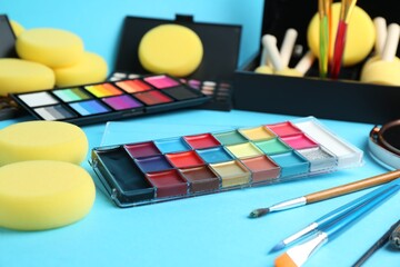 Bright face paints, brushes and sponges on light blue background, closeup