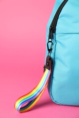 Backpack with keychain in LGBT colors on pink background, closeup. Space for text