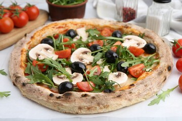 Tasty pizza with cherry tomatoes, black olives, mushrooms and arugula on white table, closeup