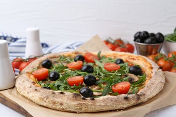 Tasty pizza with cherry tomatoes, black olives, mushrooms and arugula on white table, closeup