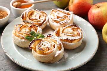Freshly baked apple roses with mint, fruits and honey on wooden table, closeup