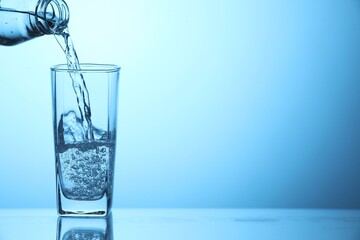 Pouring soda water from bottle into glass on light blue background, closeup. Space for text