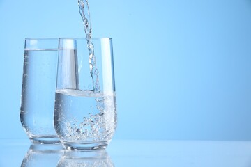 Pouring refreshing soda water into glasses on light blue background, closeup. Space for text