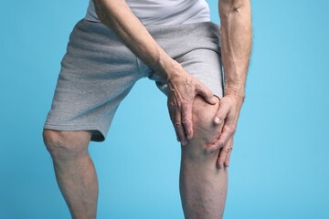 Senior man suffering from knee pain on light blue background, closeup