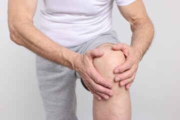 Senior man suffering from knee pain on light grey background, closeup