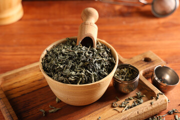 Bowl with dried green tea leaves and strainer on wooden background