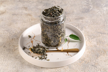 Jar and teaspoon with dried green tea leaves on white background