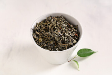 Bowl with dried green tea leaves on white background