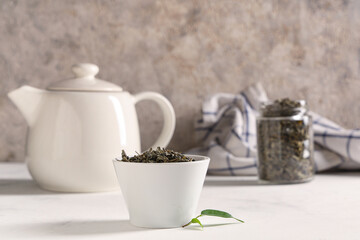 Bowl with dried green tea leaves on white background
