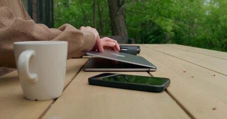 Fototapeta premium A man in casual clothes uses a laptop sitting at a table on the terrace. Close-up of his hands, an unrecognizable person